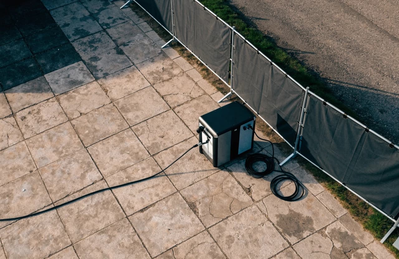A compact mobile charging station on a square near a temporary construction fence.