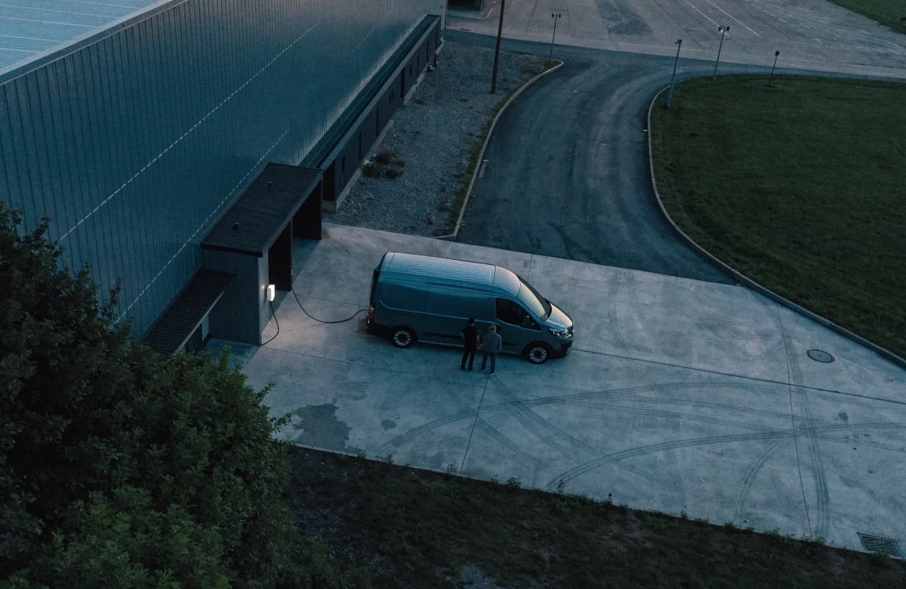 Elektrischer Liefertransporter an einer Wallbox vor einem Logistikzentrum